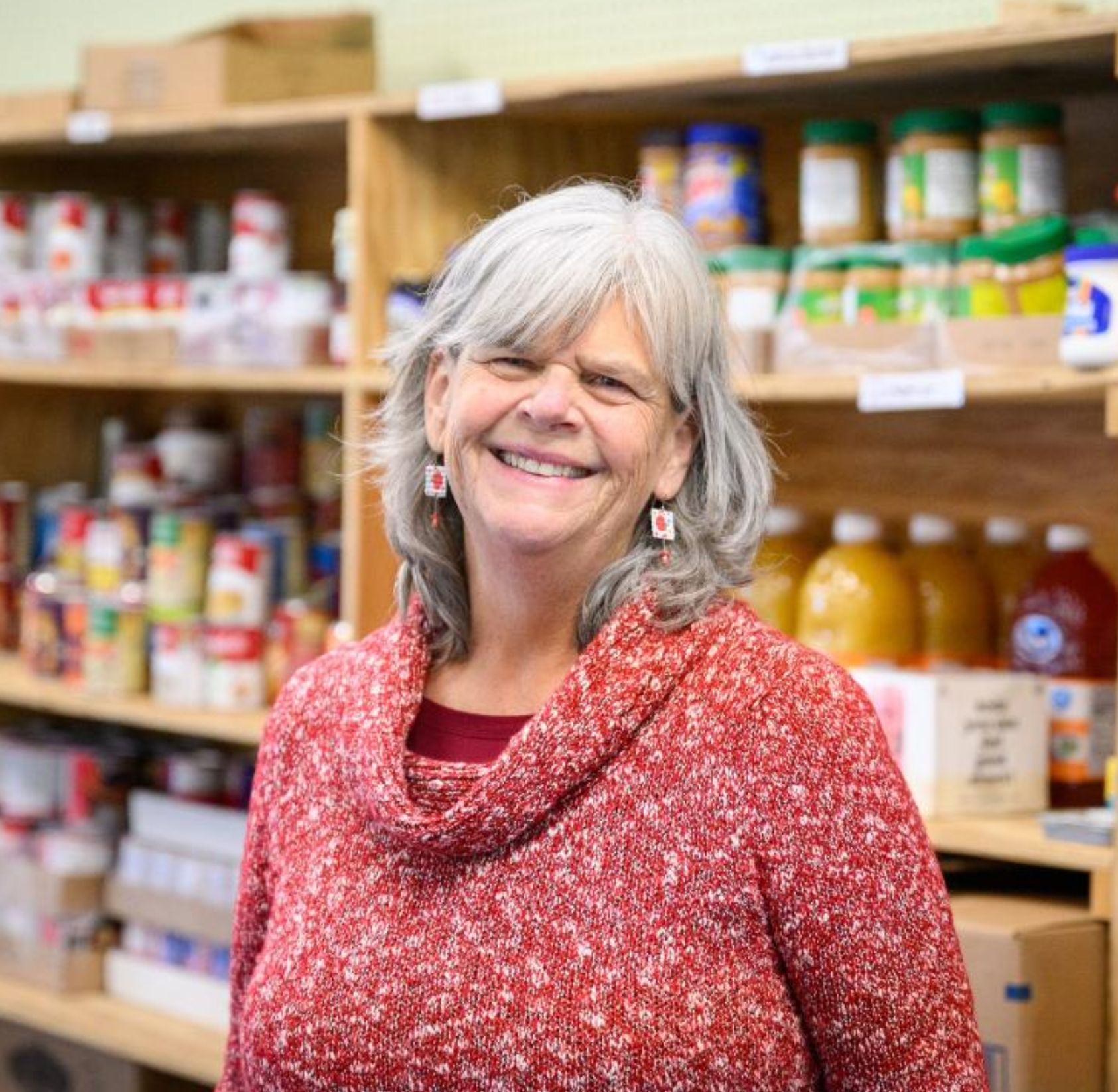 lady with gray hair smiling in red sweater in front of pantry shelves.